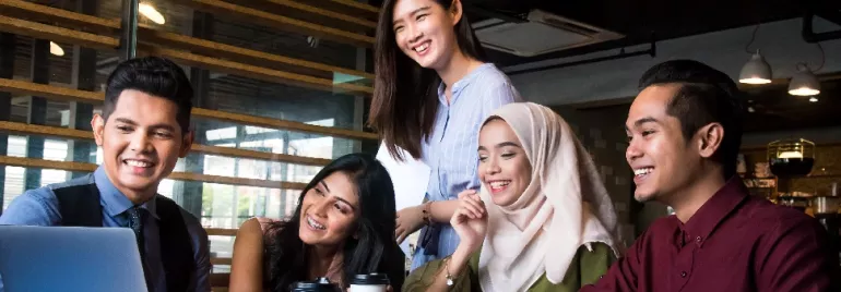 Five people smiling and looking at a laptop screen in a modern office setting.