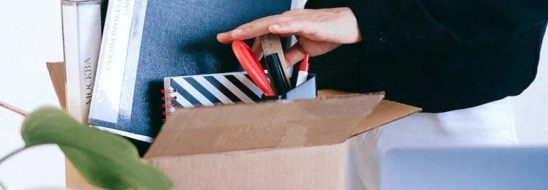 Person packing office supplies into a cardboard box.