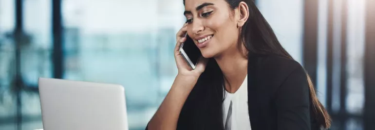 Woman smiling while talking on the phone at a laptop.