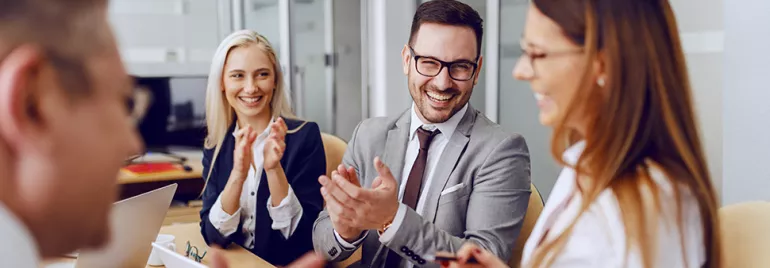 Group of professionals clapping and smiling in a meeting room.