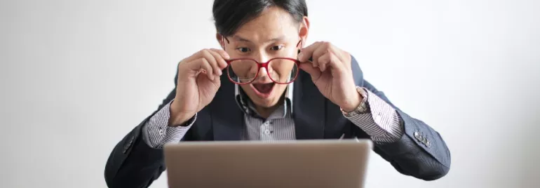 Man with red glasses looking surprised at a laptop screen.