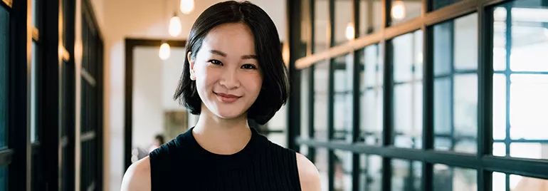 Woman with short hair smiling in a modern office with glass walls.