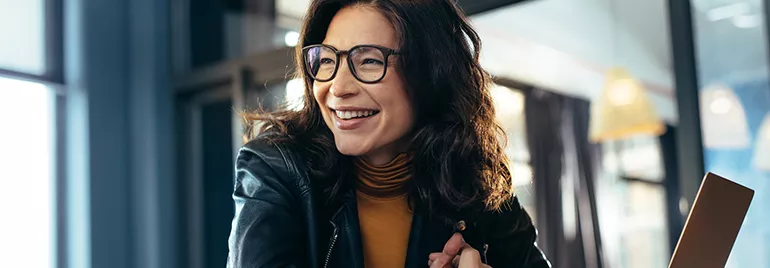Woman in glasses smiling inside a cafe.