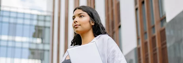 Woman holding a laptop in front of a modern building.