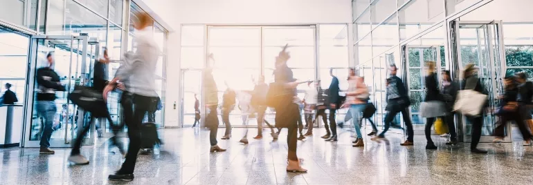 People walking through a busy lobby with glass doors.