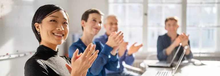 Smiling woman and colleagues clapping in a meeting room.