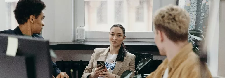 Three people conversing in an office space, one holding a smartphone.