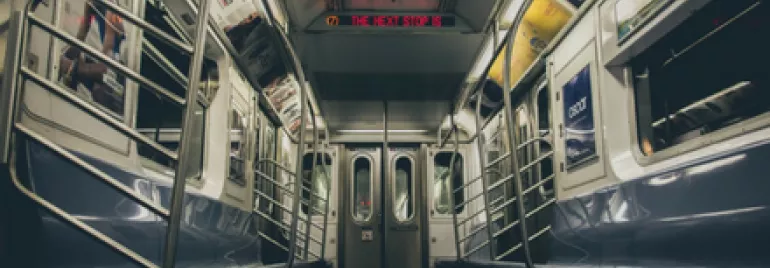 Empty subway car interior with metal poles and overhead advertisements.