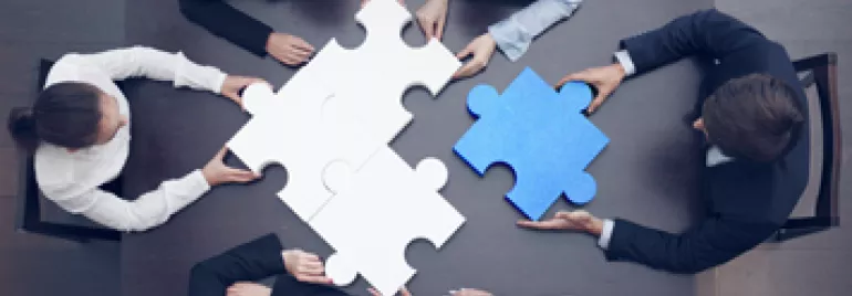 Team of business people assembling large puzzle pieces at a table.