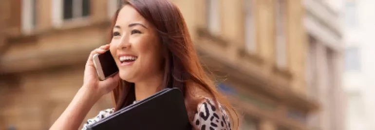 Smiling woman on phone holding a black folder, standing outdoors.
