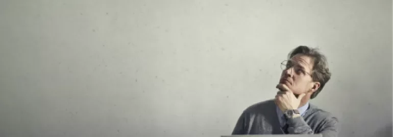 Man sitting at a desk with a laptop, thinking and looking upwards.