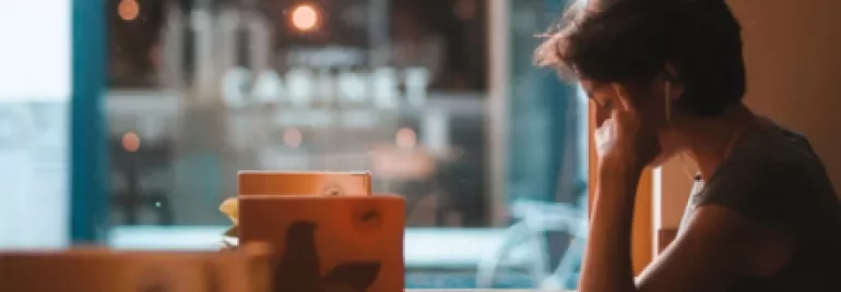 Person with earphones sitting by a cafe window, surrounded by books.