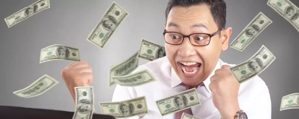 Man celebrating while dollar bills fly around him, looking excited at computer.