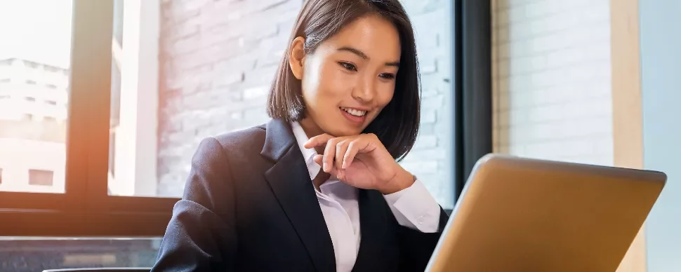 Businesswoman smiling and using a laptop at a desk.