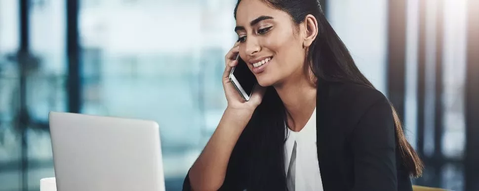Woman smiling while talking on the phone at a laptop.