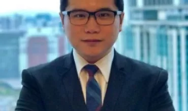 Man in suit with glasses standing in front of a cityscape.