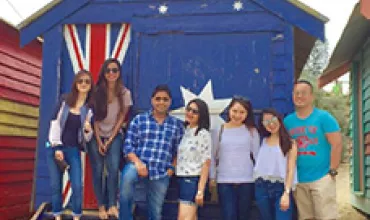 Group of people posing in front of a blue beach hut with Australian flag design.