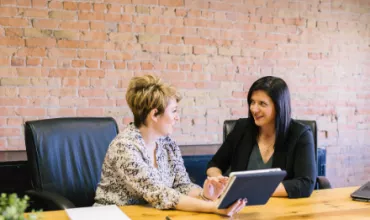 Two women discussing a project with a tablet at a conference table.