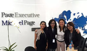 Four colleagues smiling in an office with 'Page Executive' sign, world map in the background.