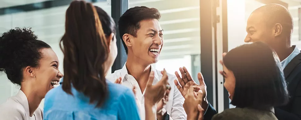 Group of diverse colleagues laughing and clapping in an office.