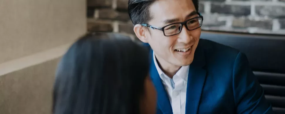 A man in a blue suit and glasses smiles during a meeting.
