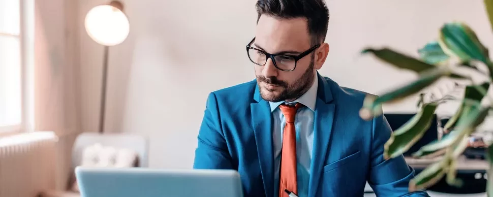 Man in blue suit working on a laptop in a modern office.