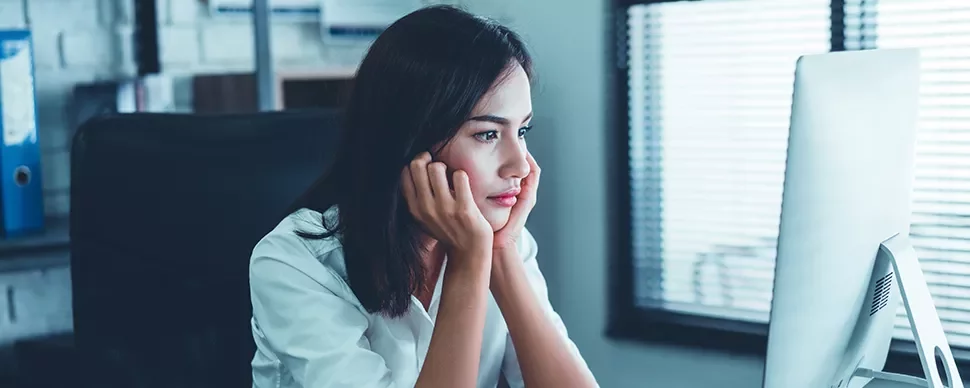 Woman in a white shirt looking at a computer screen, appearing thoughtful.