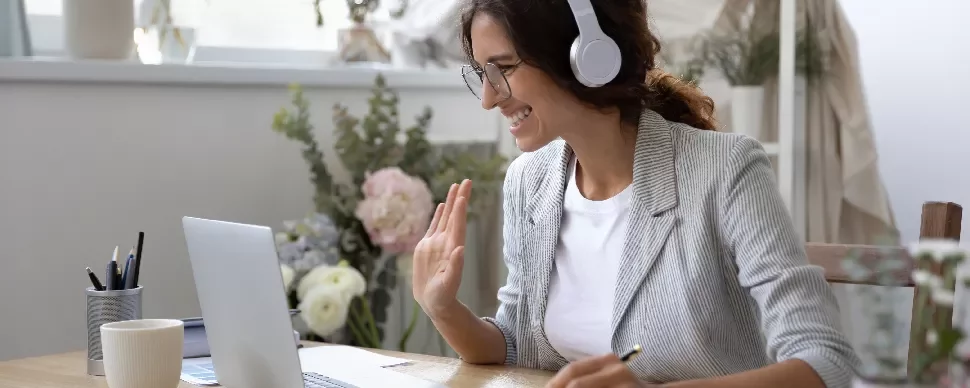 Woman wearing headphones smiling at laptop screen during a video call.
