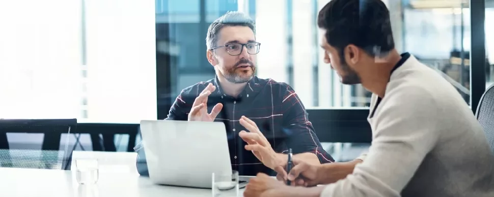Two men having a discussion at a table with a laptop.
