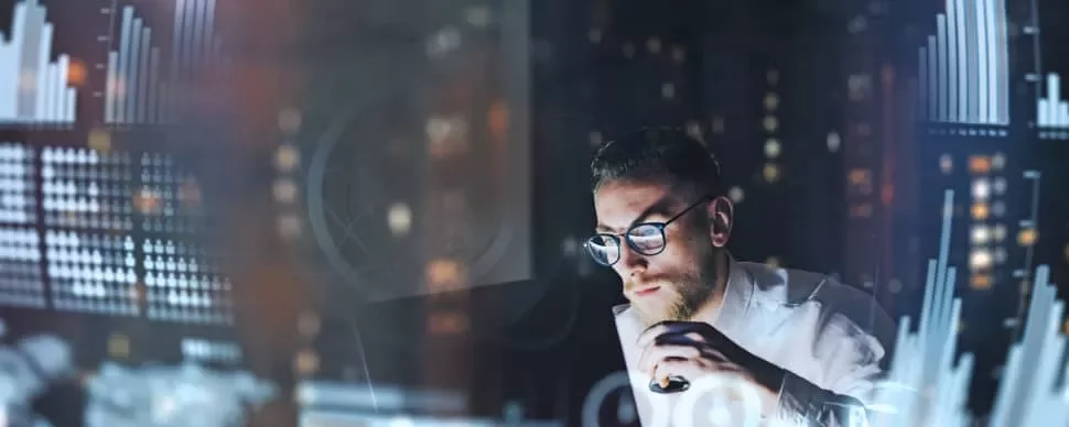 Man in glasses analyzing digital data with graphs around him.