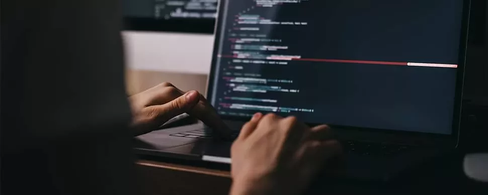 Hands typing code on a laptop keyboard.