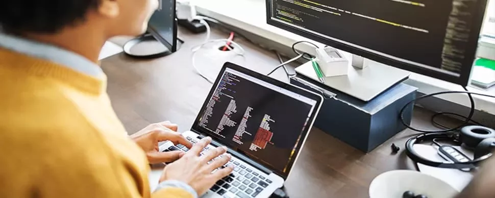 Person coding on a laptop with additional screen nearby.