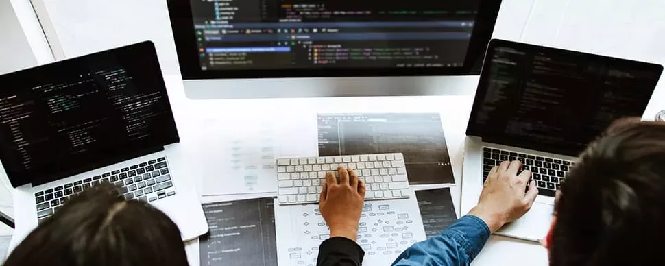 People working on laptops with code on screens, collaborating around a desk.