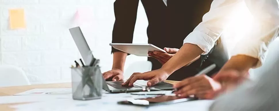People collaborating at a desk with laptops and tablet.