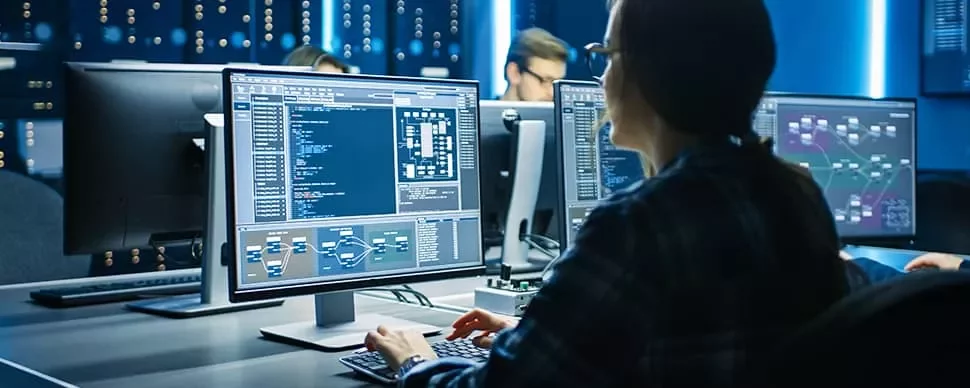 Person analyzing data on multiple computer monitors in a tech office.