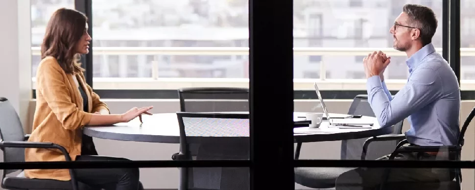 Two professionals having a discussion at a round table in an office setting.