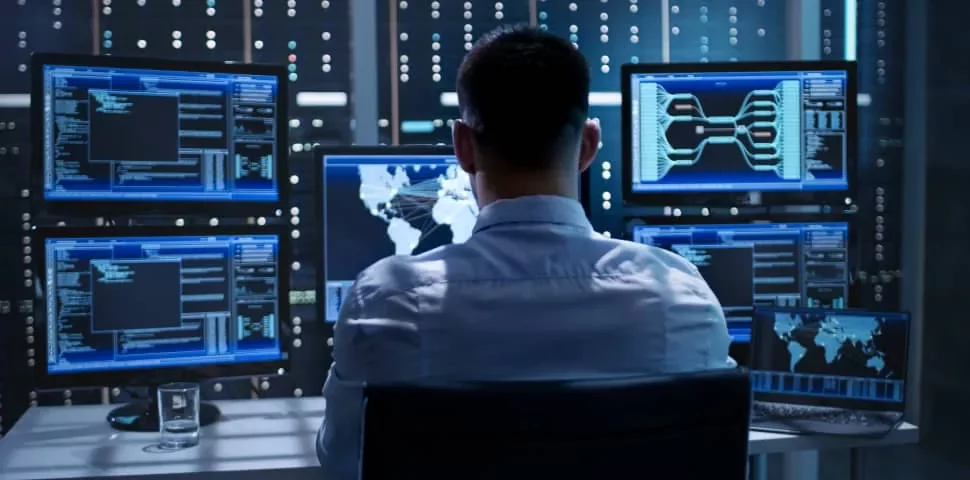 Person in front of multiple monitors displaying data and maps in a control room.