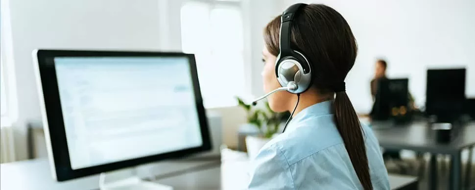Woman with headset working at a computer in an office setting.