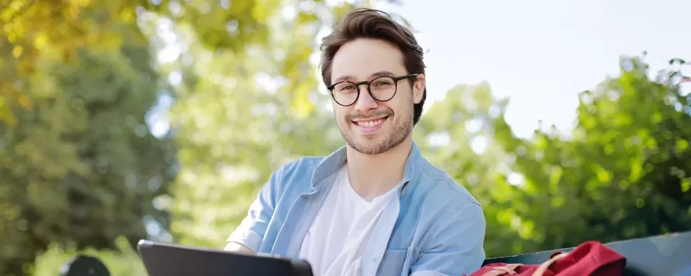 Person with glasses smiling outdoors on a sunny day.