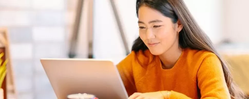 Woman in orange sweater using a laptop, seated indoors.