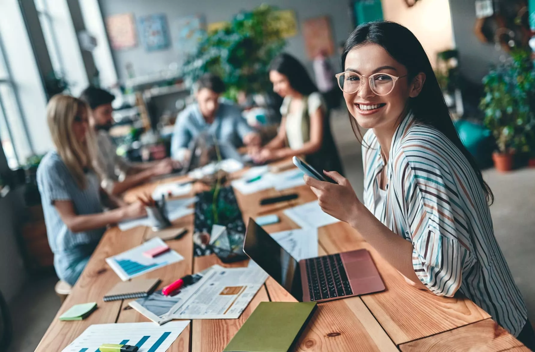 Smiling woman with smartphone in a busy office meeting.