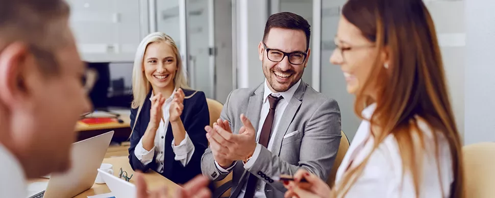 Group of professionals clapping and smiling in a meeting room.