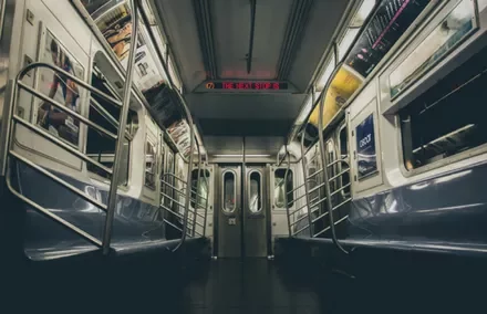 Empty subway car interior with metal poles and overhead advertisements.