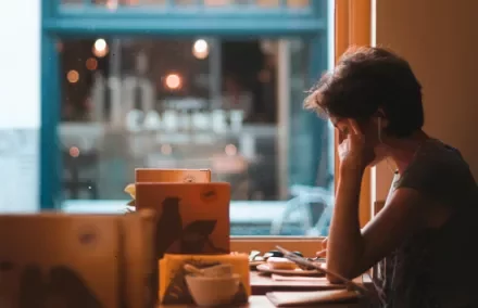 Person with earphones sitting by a cafe window, surrounded by books.